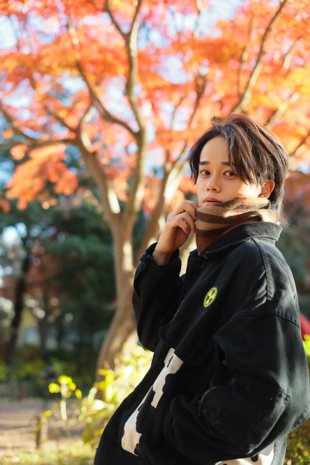 紅葉の下でマフラーを口元に寄せるほまれの屋外ポートレート