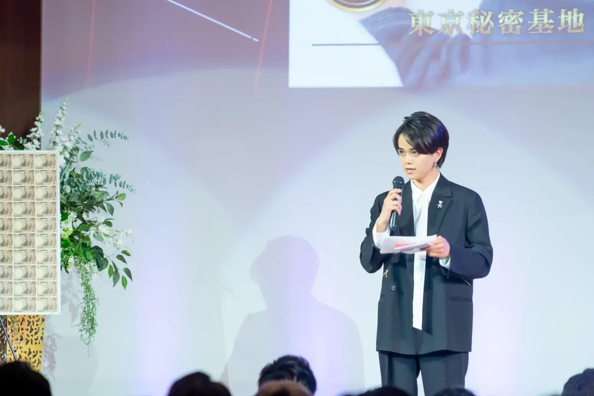 最高セラピストグランプリ2023 表彰式の壇上でスピーチする東京秘密基地のほまれ。背景のスクリーンに東京秘密基地のロゴ